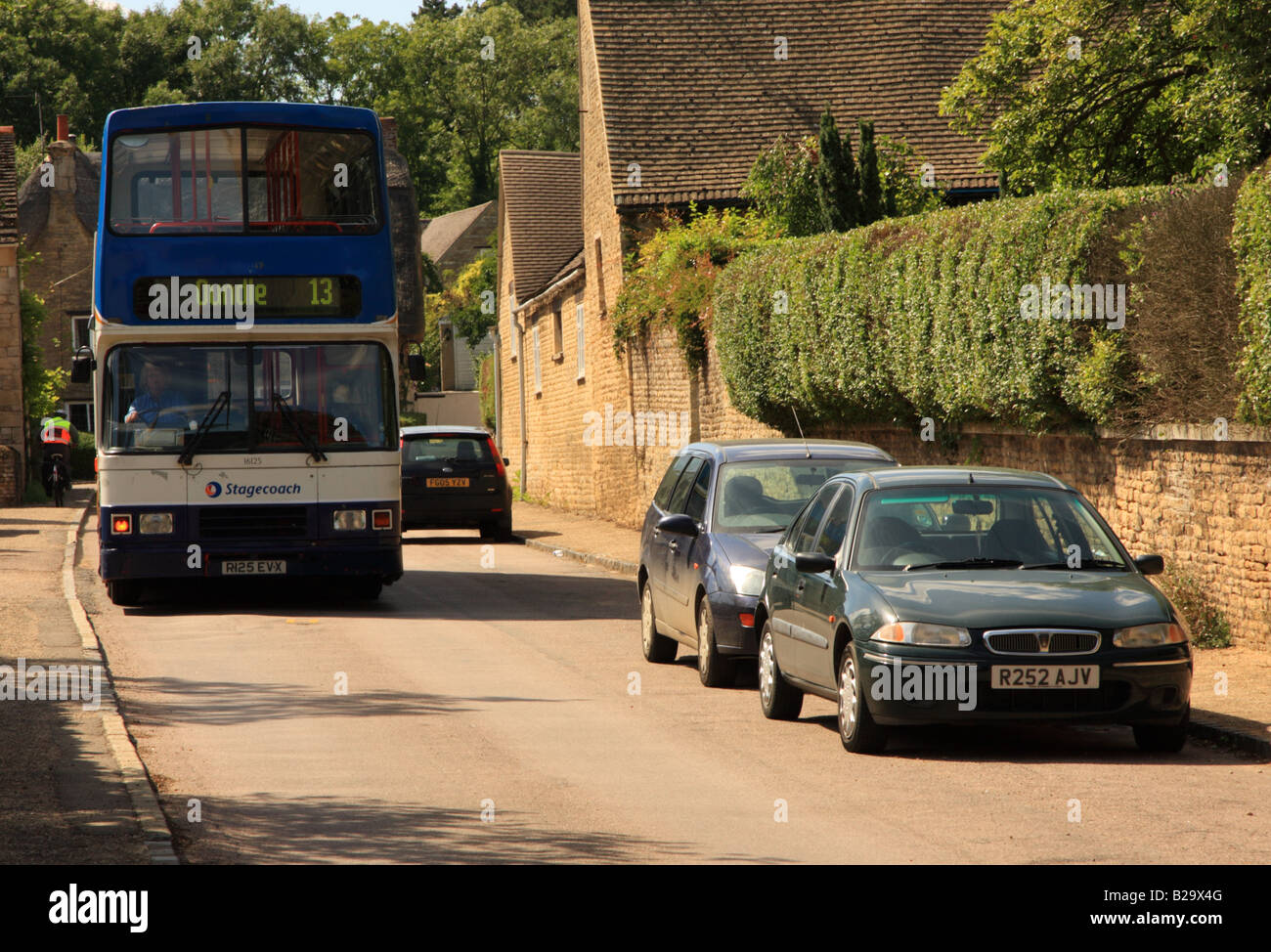 A very large bus squeezes down a tiny village street Stock Photo