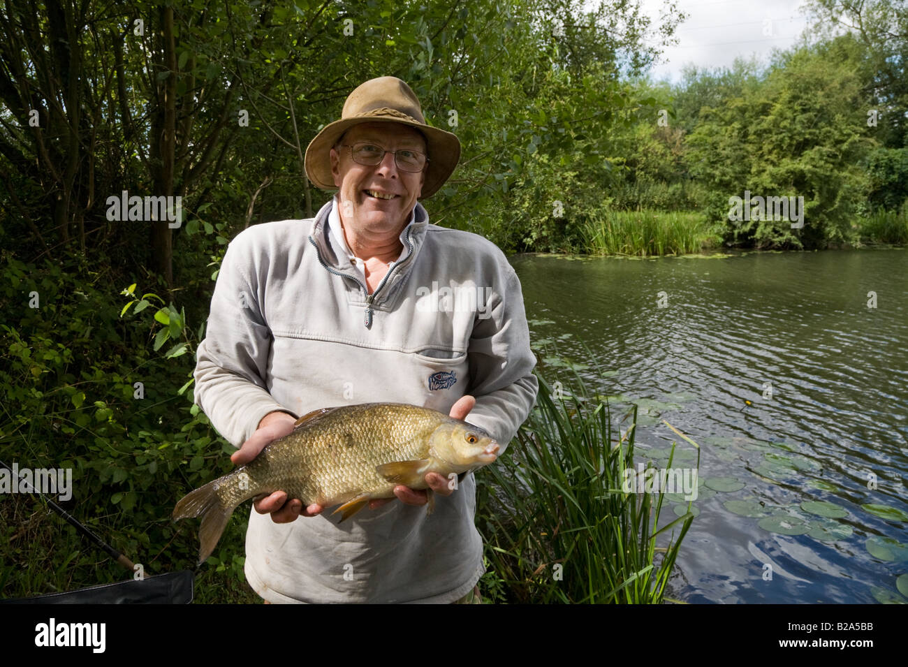 A proud delighted smiling man, a coarse angler holds a fish caught from Farlows Lake Iver Buckinghamshire UK Stock Photo