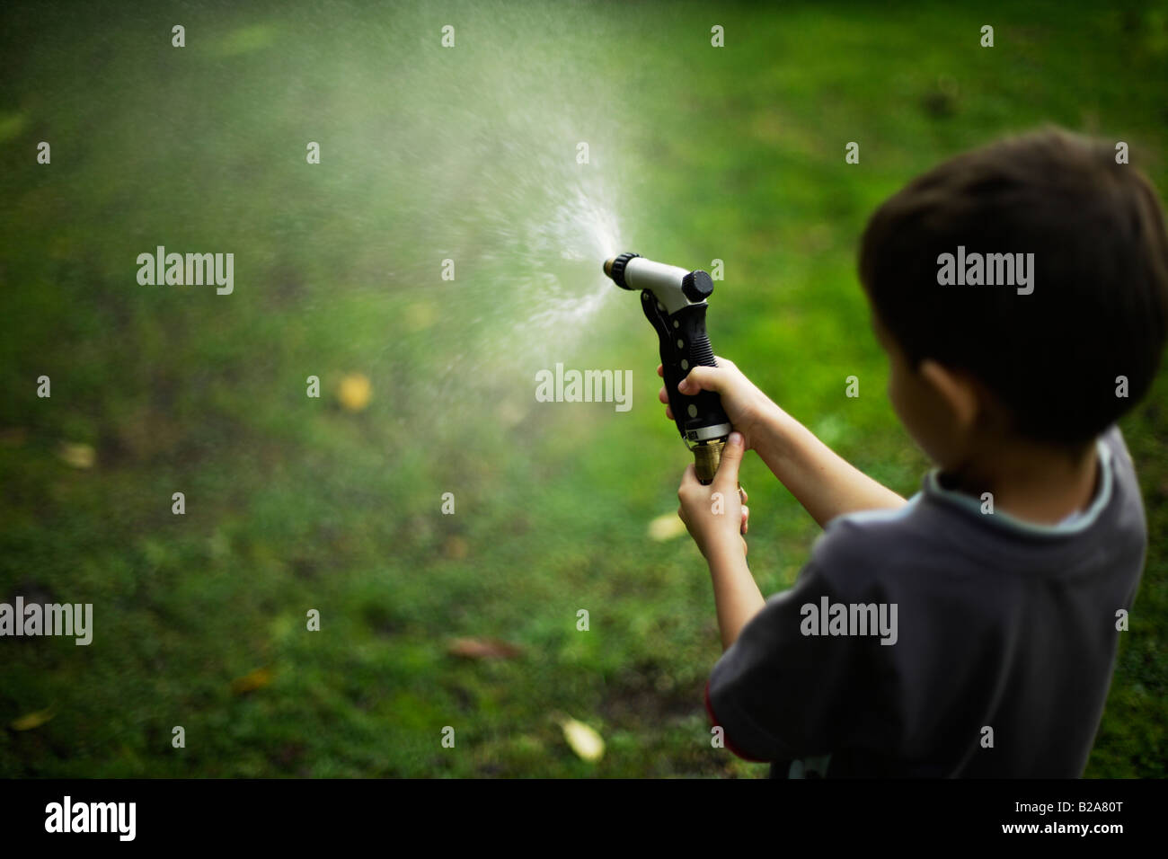 Six year old biy sprays lawn with hose and brass spraygun Mixed race indian ethnic and caucasian Stock Photo