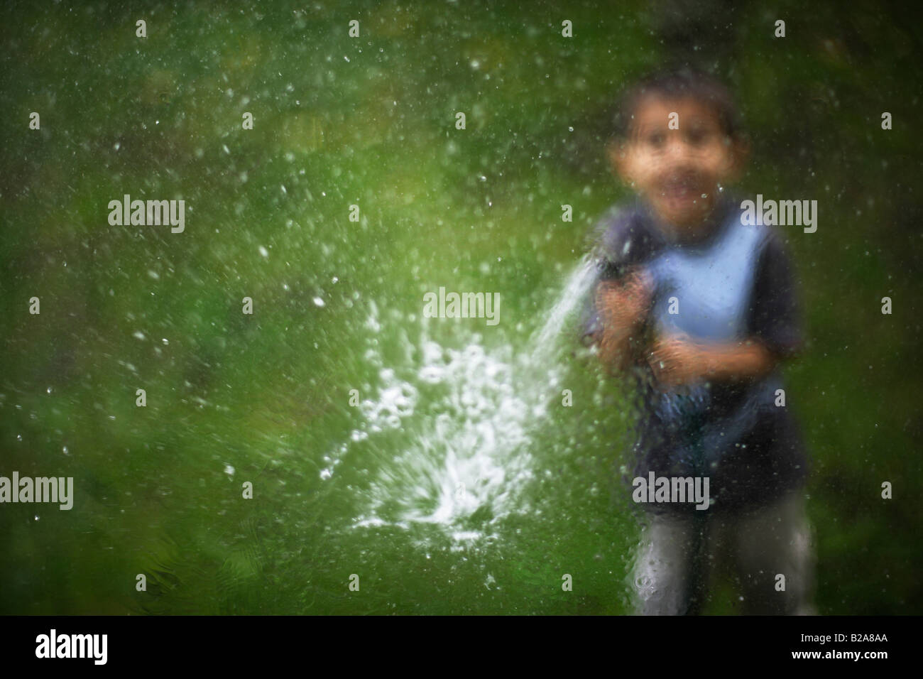 Hosepipe sprayed at a glass window Six year old boy Mixed race indian ethnic caucasian Stock Photo