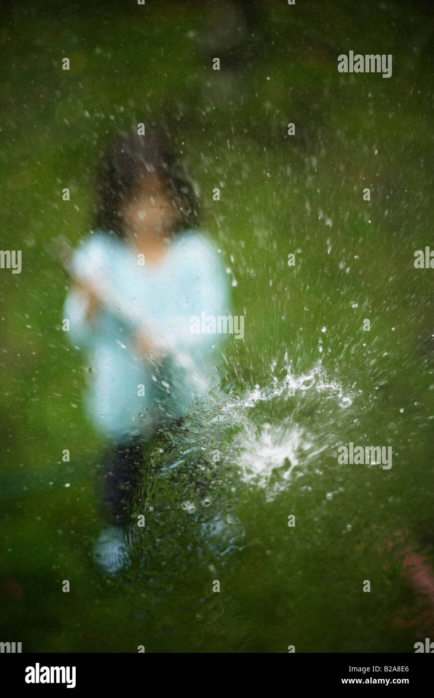 Hosepipe sprayed at a glass window Five year old girl Mixed race indian ethnic caucasian Stock Photo