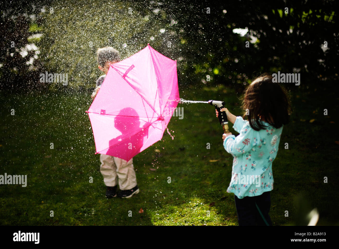 Boy aged six years shelters behind pink umbrella Stock Photo