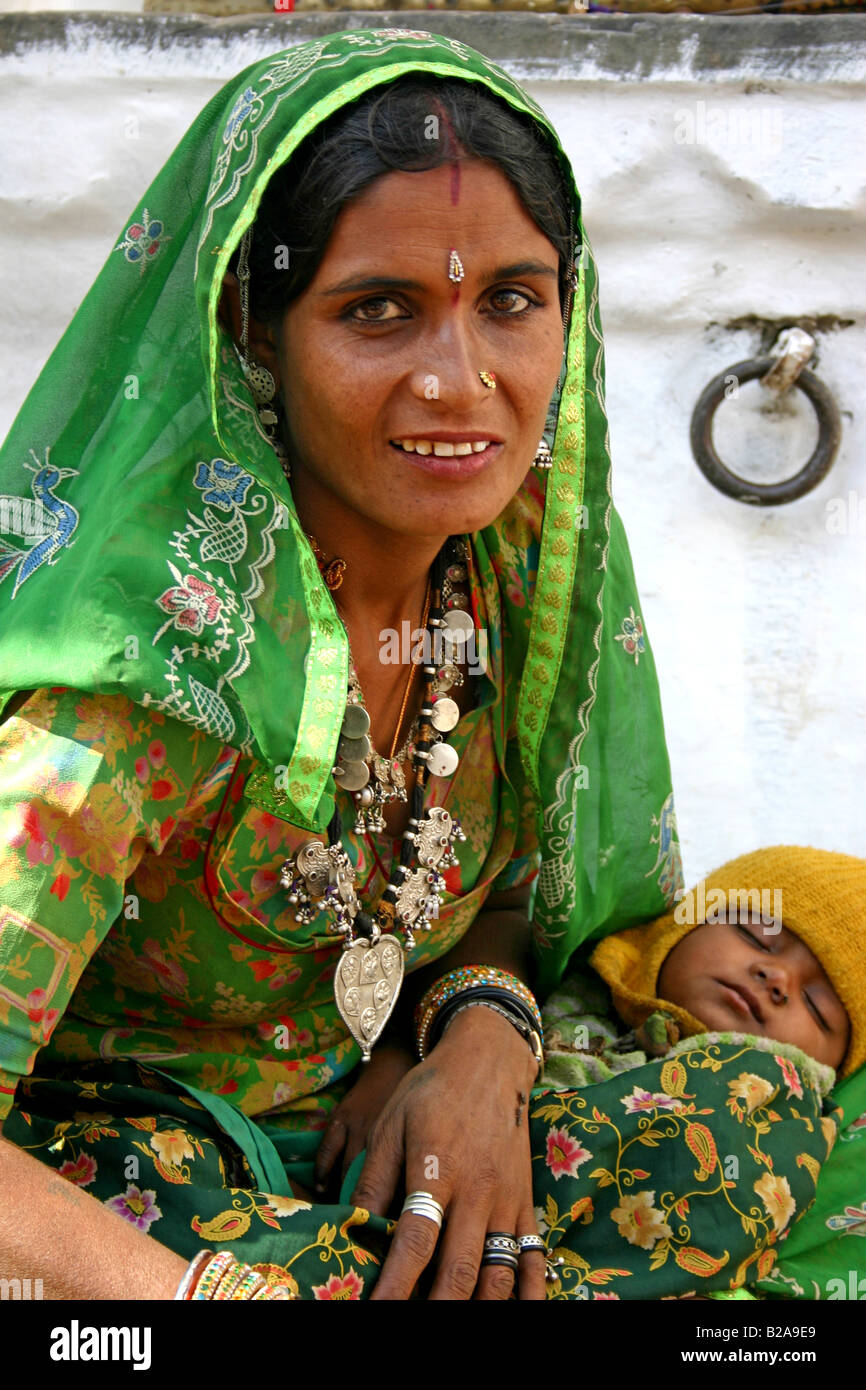 Portrait of a beautiful Rajasthani woman in a decorated green sari holding sleeping baby in Udaipur Stock Photo