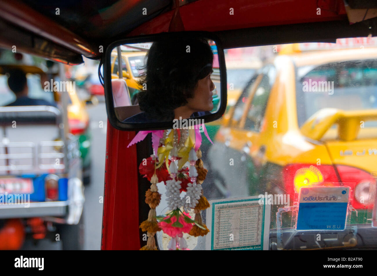 A driver is reflected in the rearview mirror of an Auto rickshaw taxi, commonly known as Tuk Tuk in Bangkok Thailand Stock Photo