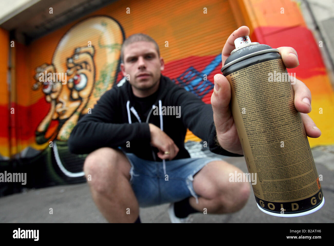A graffiti artist holds up a spray paint can next to his work in ...