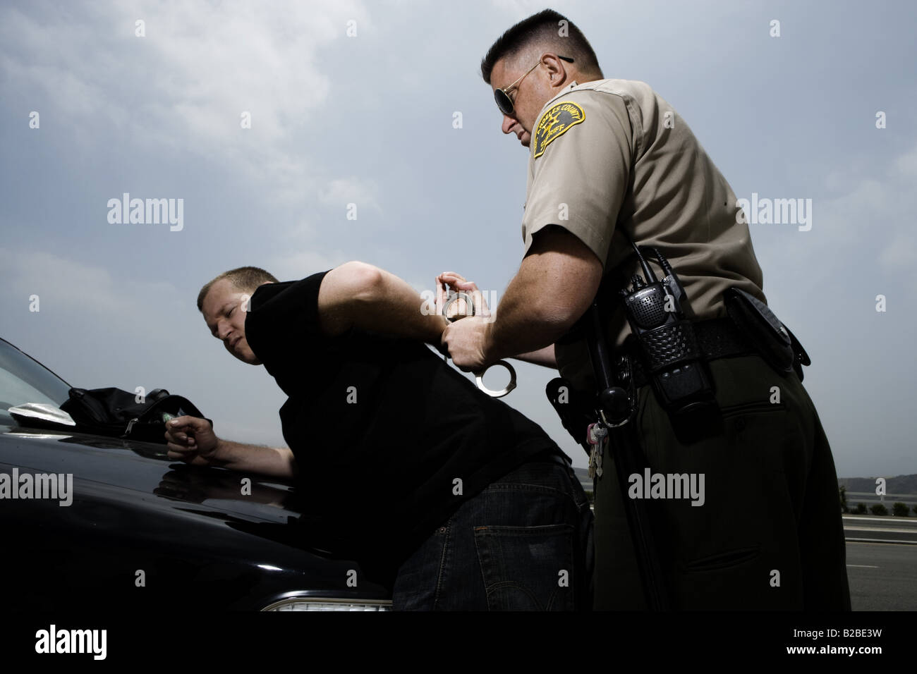 Man being handcuffed by police officer on hood of black car Stock Photo