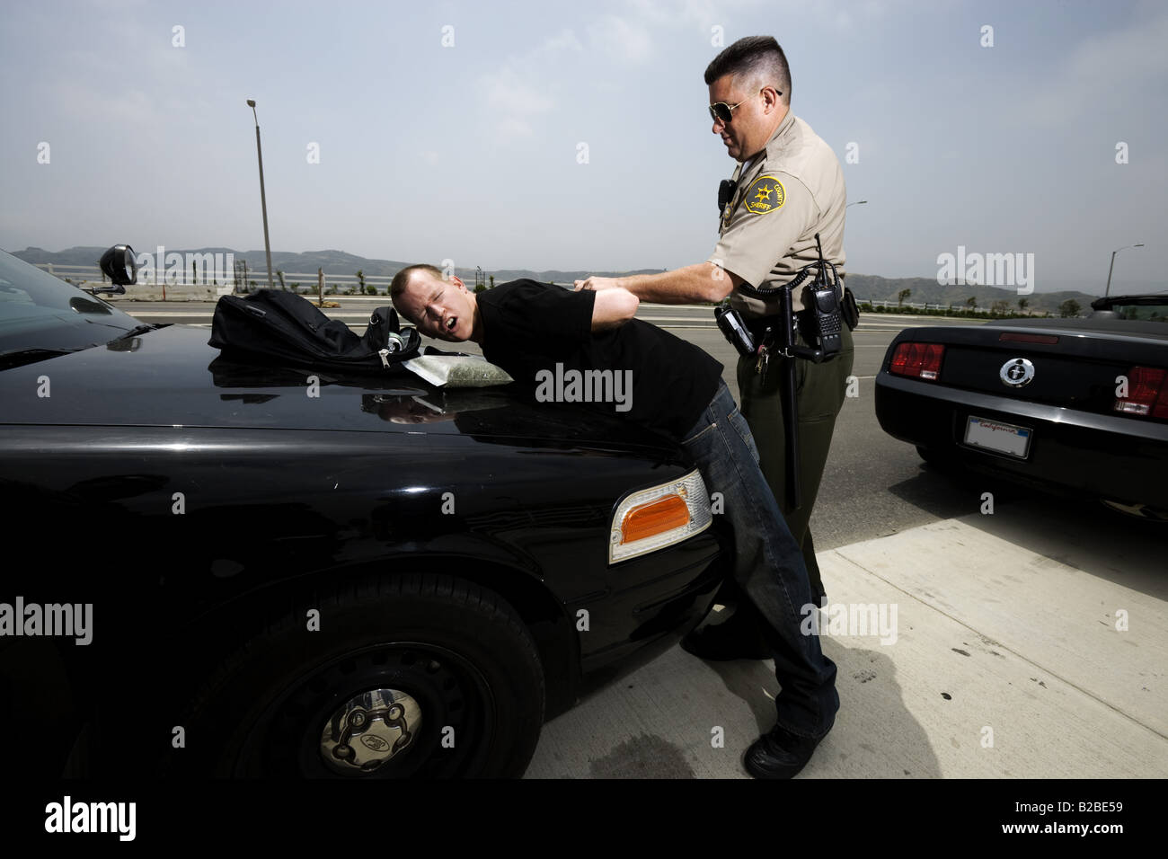 Man being handcuffed by police officer on hood of black car Stock Photo