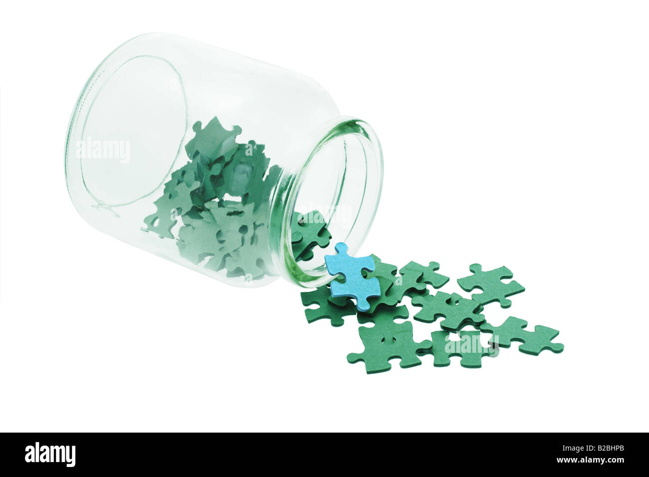 Blue piece among all green jigsaw puzzles spilled from glass bottle Stock Photo