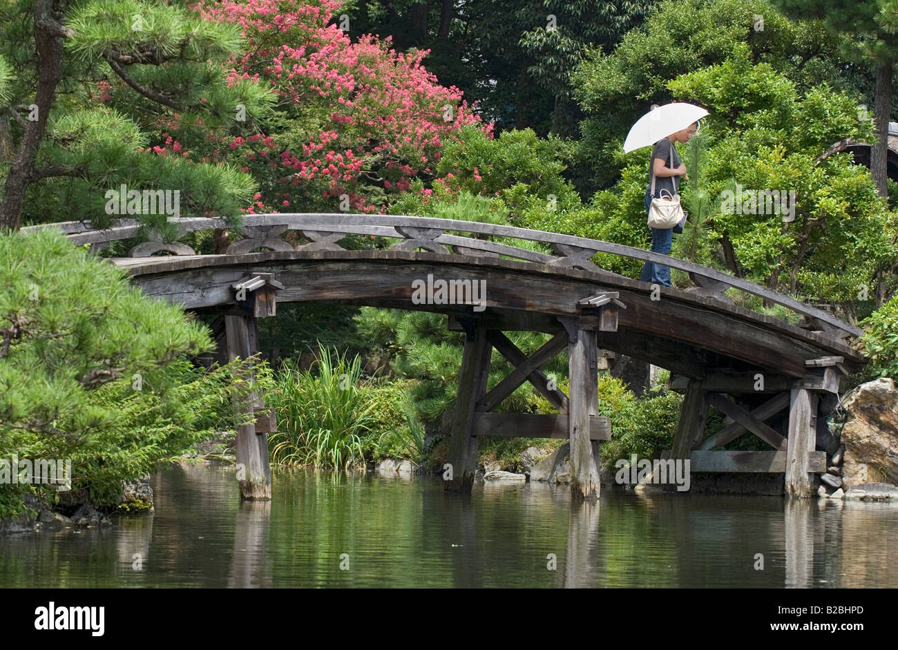 Person carrying umbrella walking across an old wooden arched bridge at Shoseien Garden in Kyoto Stock Photo