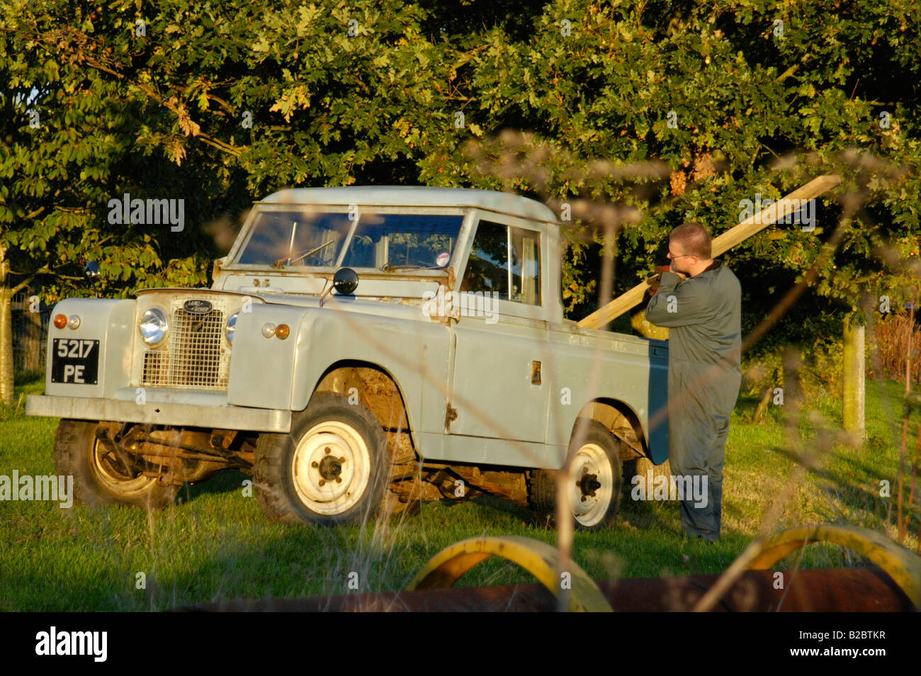 Workman in overall loading a timber beam into the back of a historic 1963 Landrover Series 2a truckcab in very original and ... Stock Photo