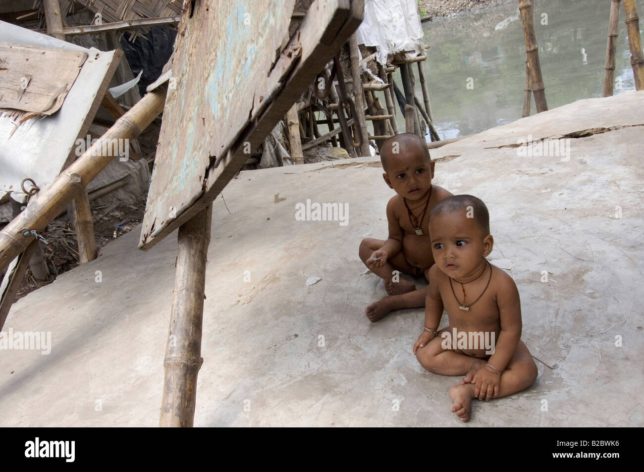 Infants sitting under the rubble of an old hut in the slums of Topsia. Behind them, the sewer of Topsia, reeking of methane gas Stock Photo