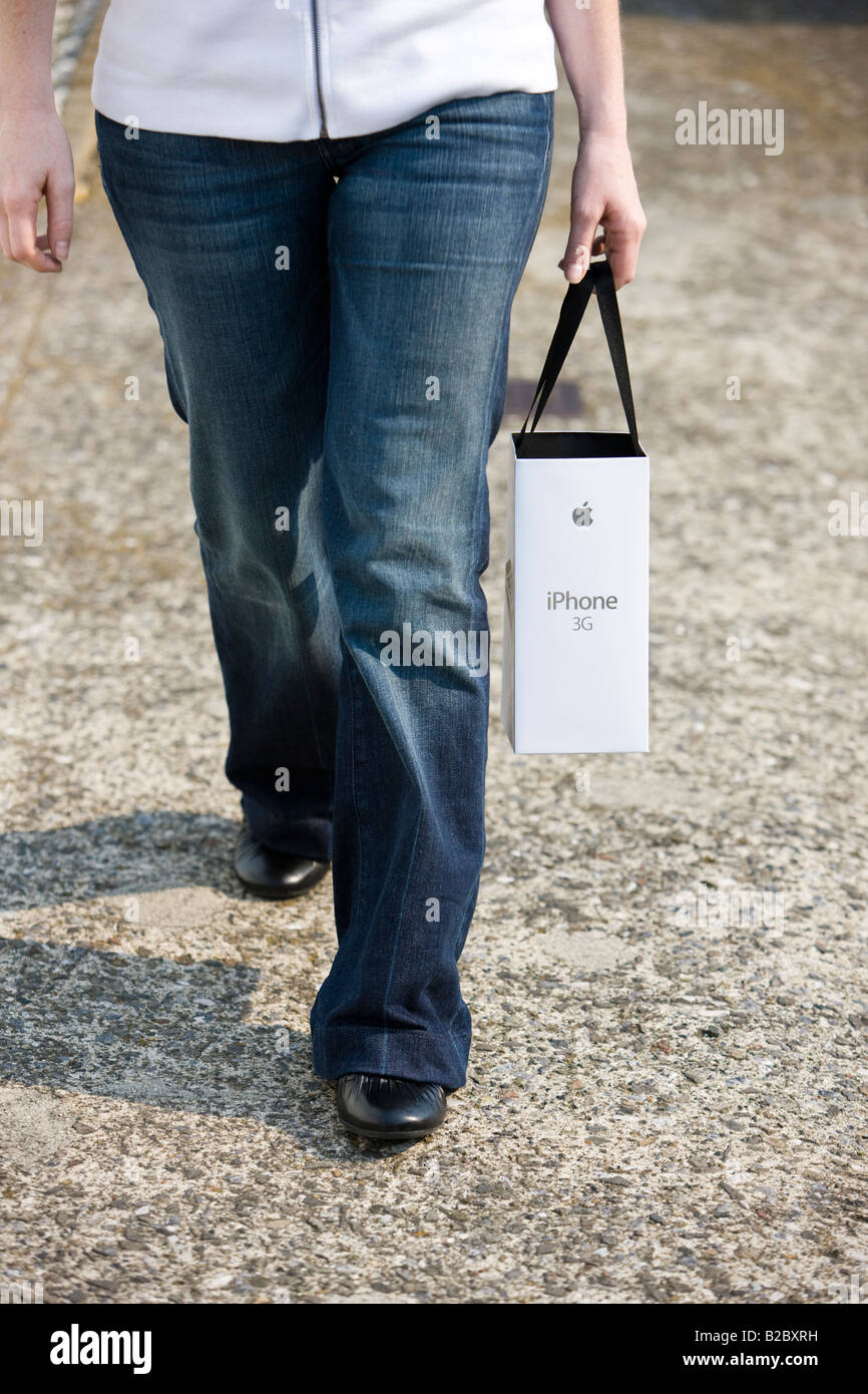 A shopper returns from purchasing an Apple 3G iPhone with product and bag in hand Stock Photo