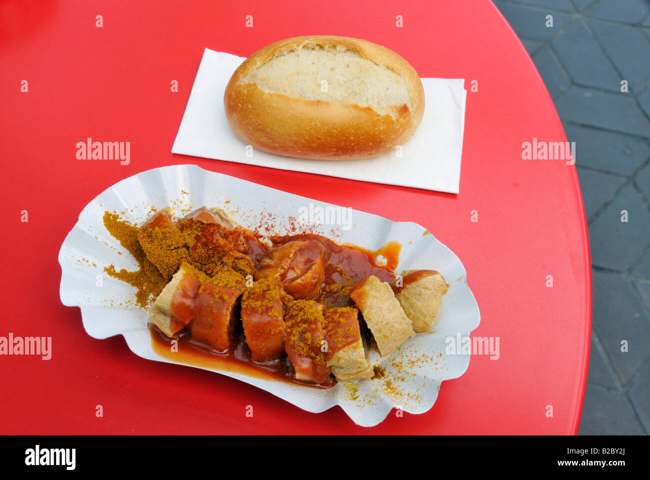 Currywurst, curried sausage and bun on a red table Stock Photo