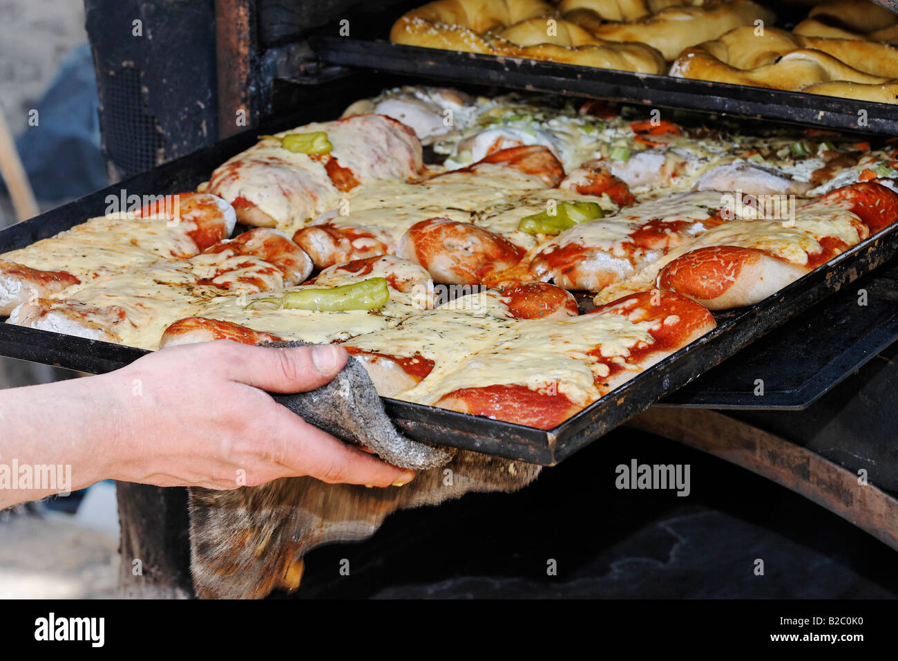 Hand pulling a baking tray filled with pizza breads out of a rustic