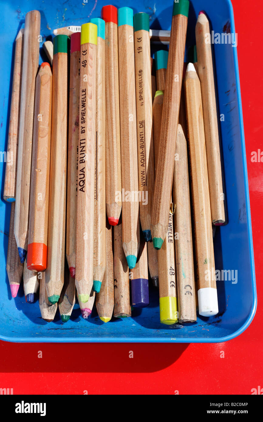 Coloured crayons in a blue bowl on a red backing Stock Photo