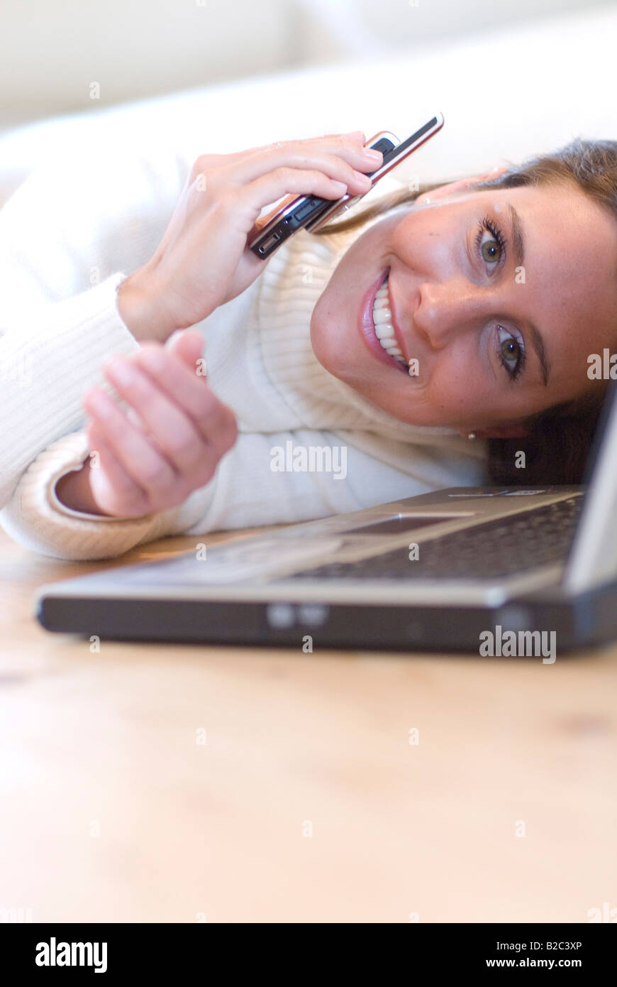 young woman lying on the livingrooms floor, working with the notebook and phoning Stock Photo
