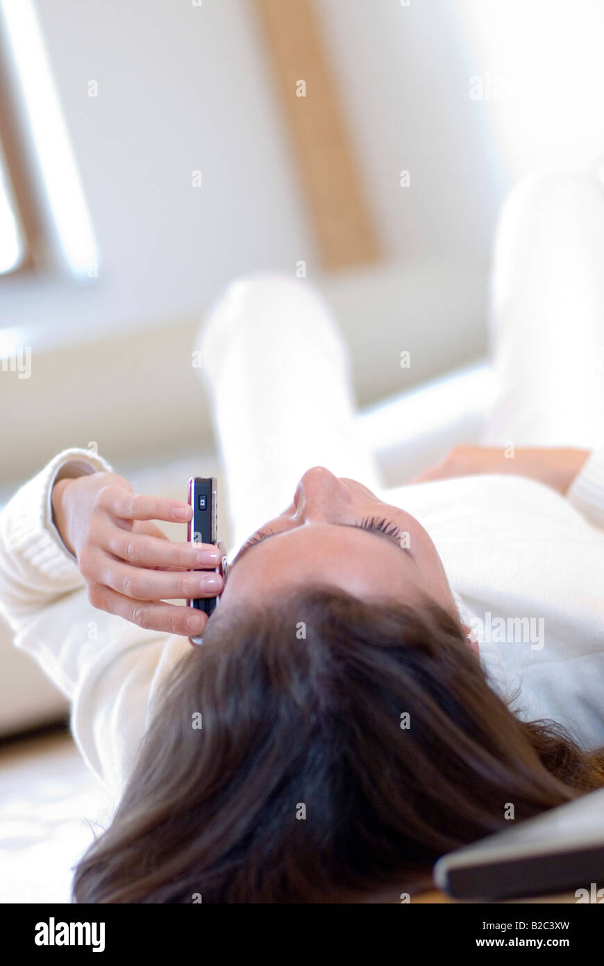 young woman lying on the livingrooms floor and phoning Stock Photo