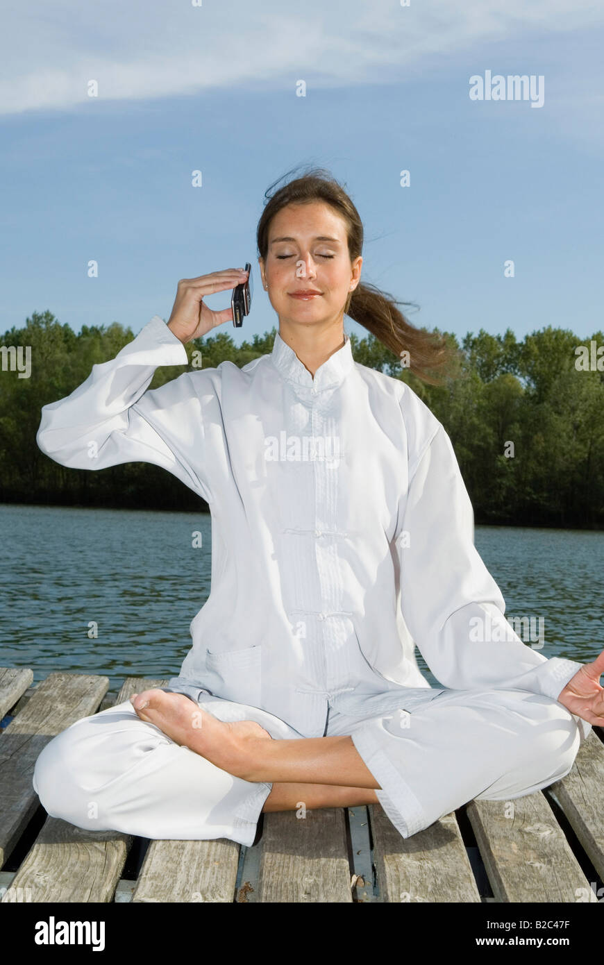 Woman practising Yoga, half lotus pose, Ardha Padmasana, Mudra and phoning Stock Photo