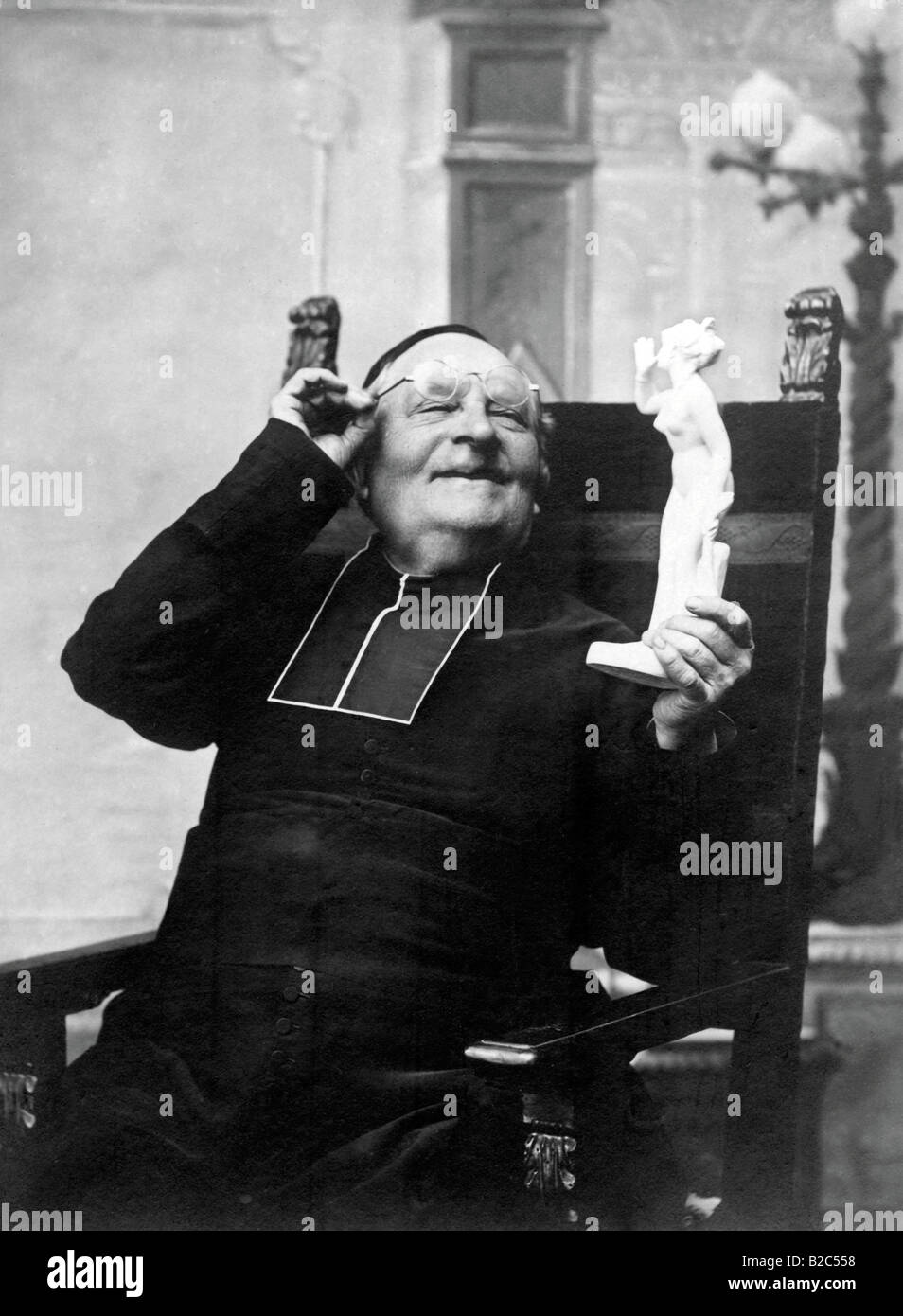 Priest looking at a figurine of a woman, historical photo, circa 1930 Stock Photo