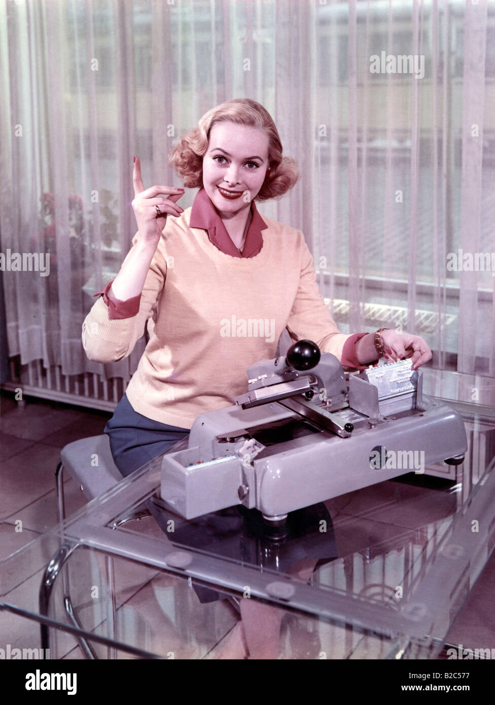 Woman sitting in front of a typewriter, historic picture from about 1955 Stock Photo