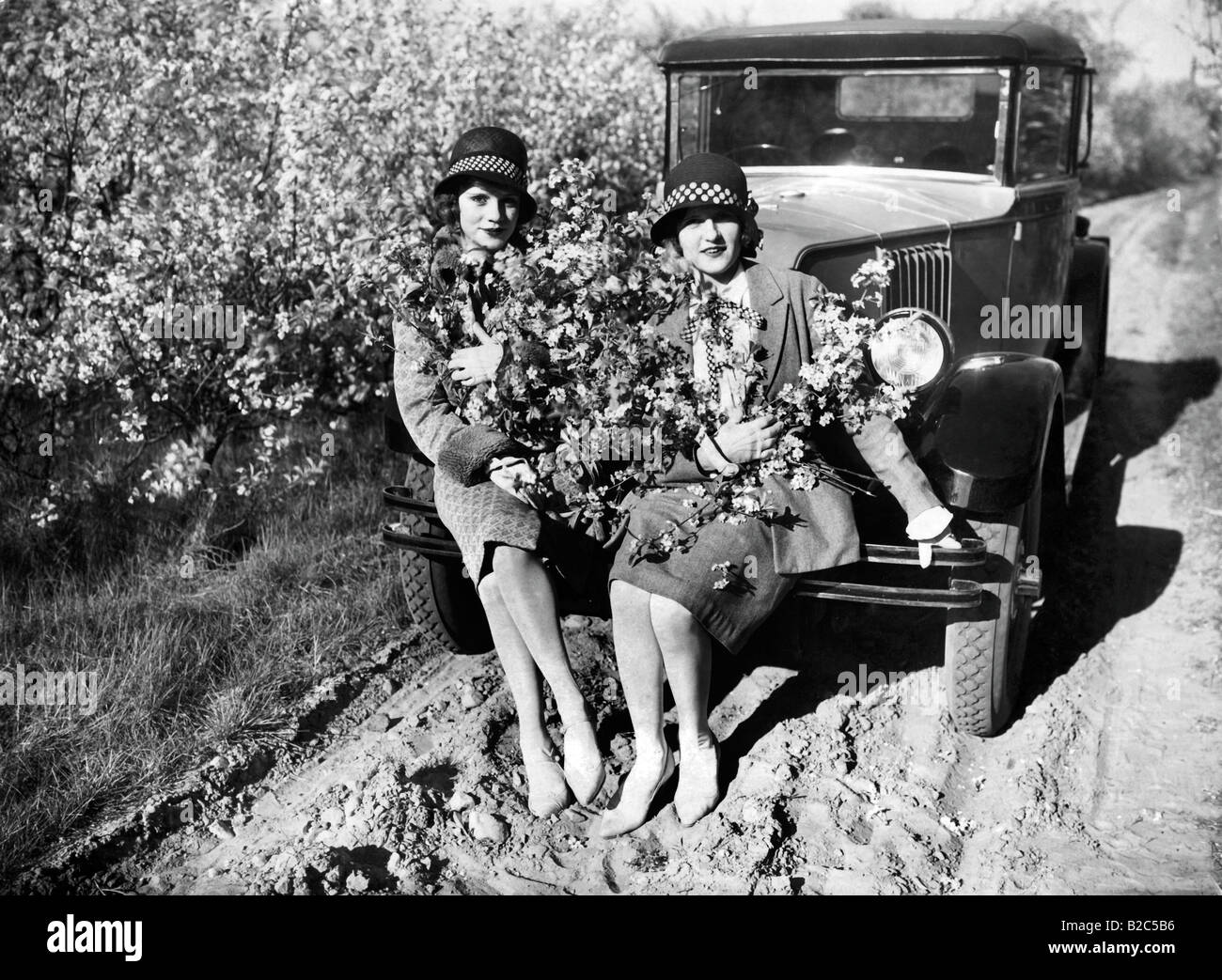 Two women with flowers sitting on a car, historical photo, circa 1920 Stock Photo