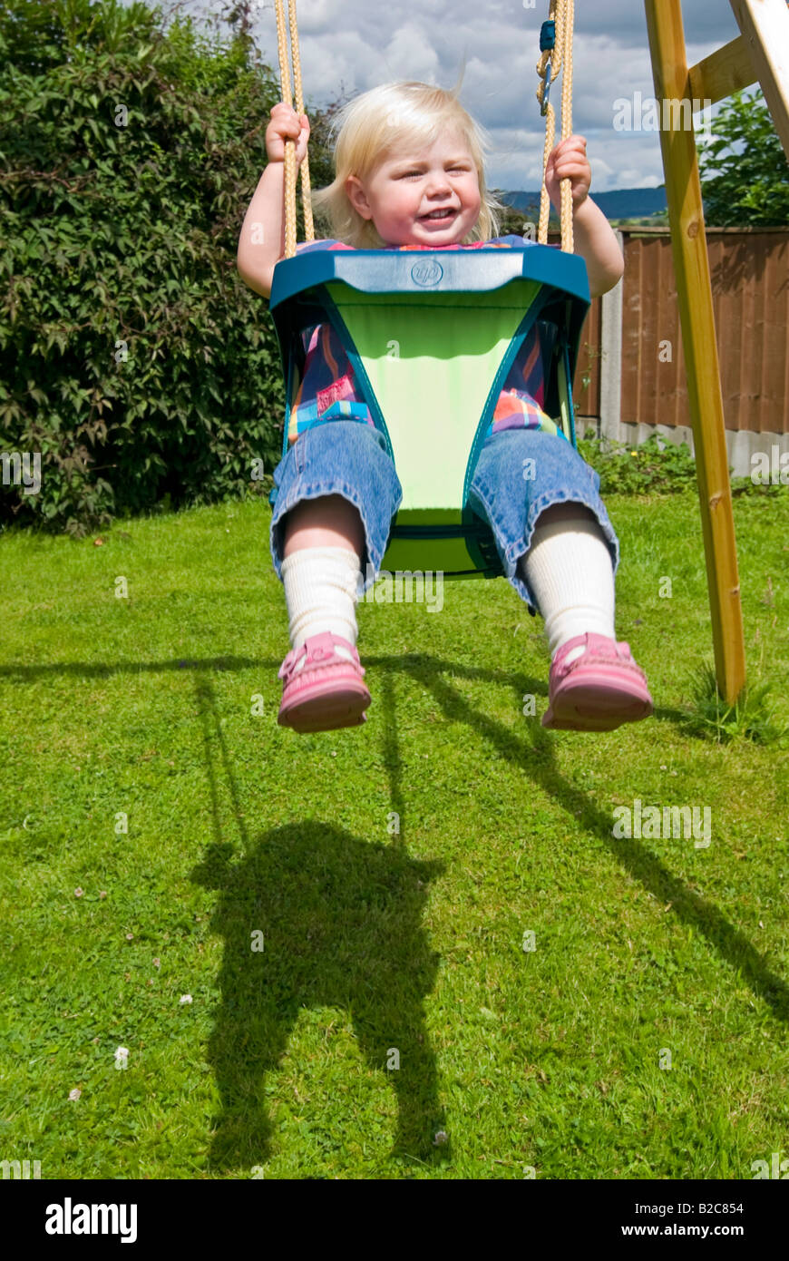 Vertical portrait of an 18month old little girl having great fun playing on her swing outside