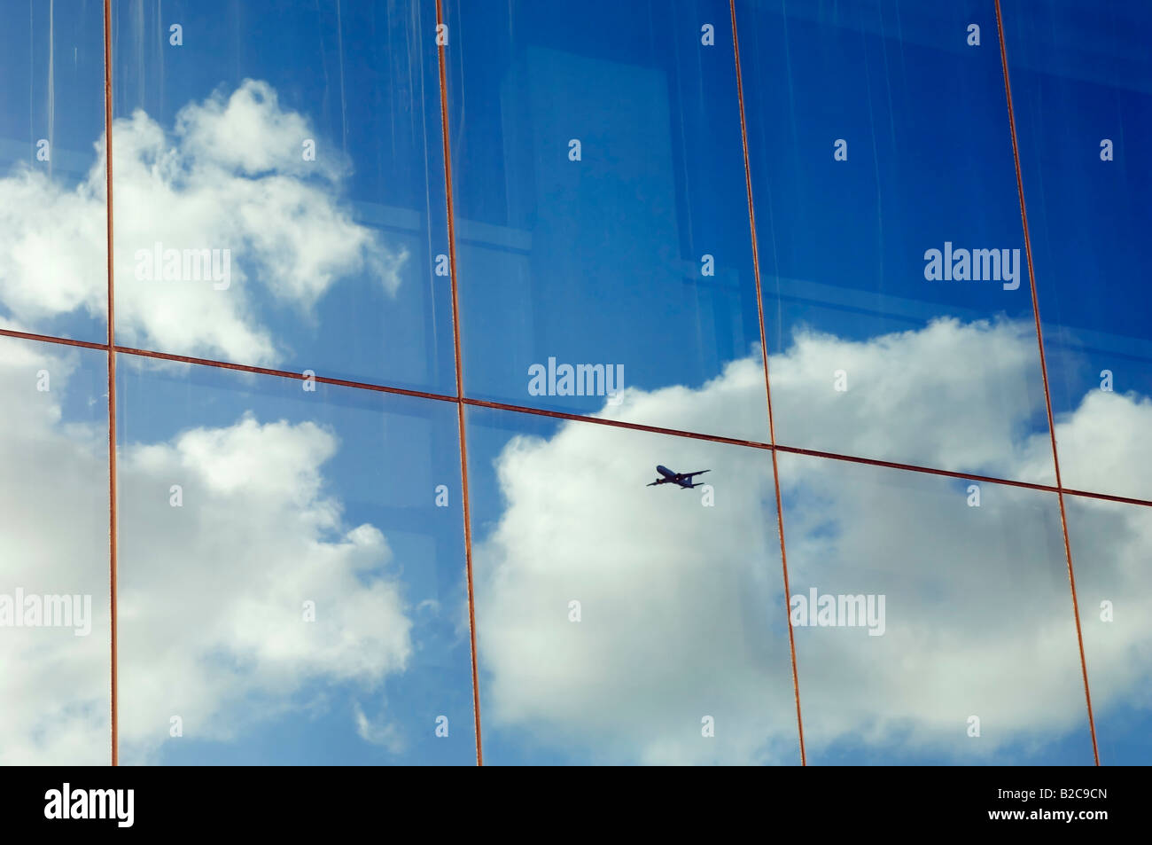Airplane sky and clouds reflected in the window of a modern office building Stock Photo