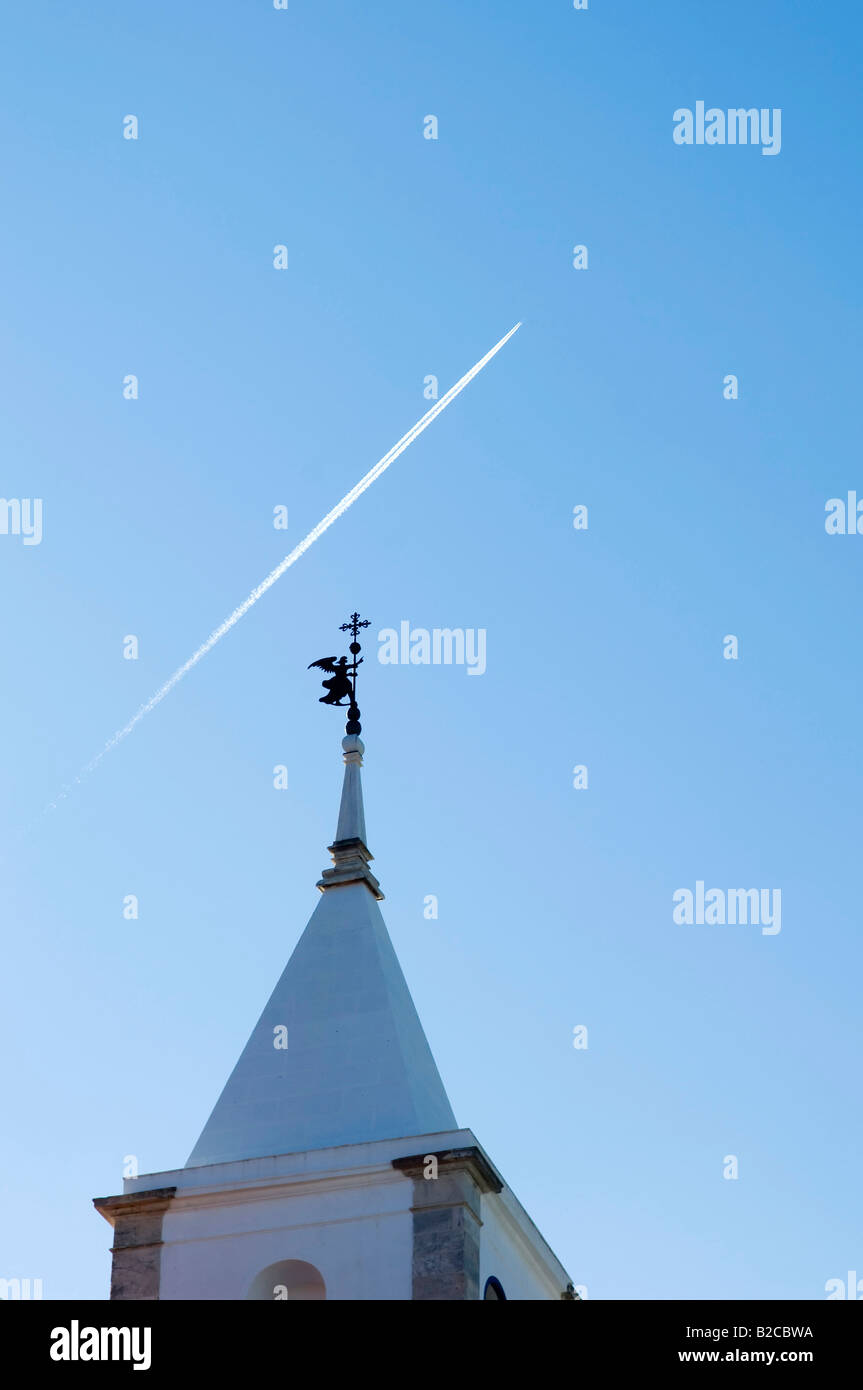 Belfry tower with an angel weather vane pointing to the sky cruised by a jet plane Stock Photo