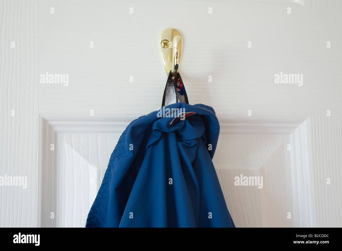 Blue coat hanging on brass hook on back of a white wooden door. England UK Stock Photo