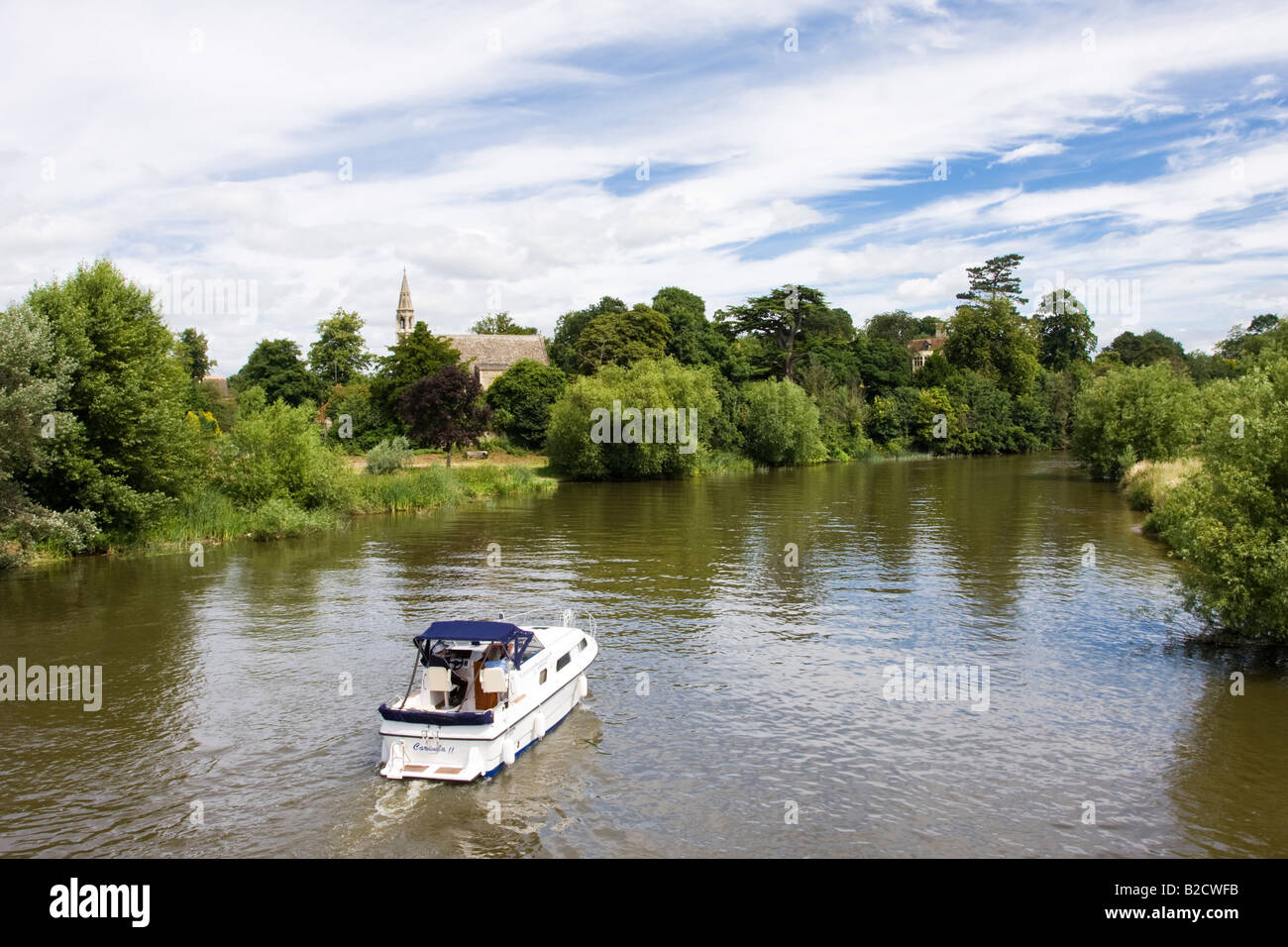 A Motor Cruiser passes Clifton Hampden on the River Thames Oxfordshire Stock Photo
