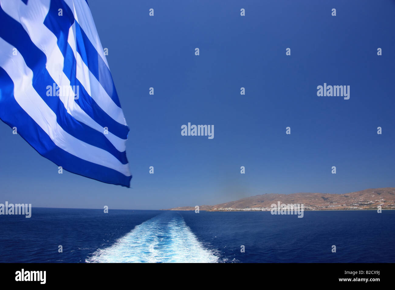 Watching the ship wake and the Greek flag and the Greek island of Tinos in the far Stock Photo