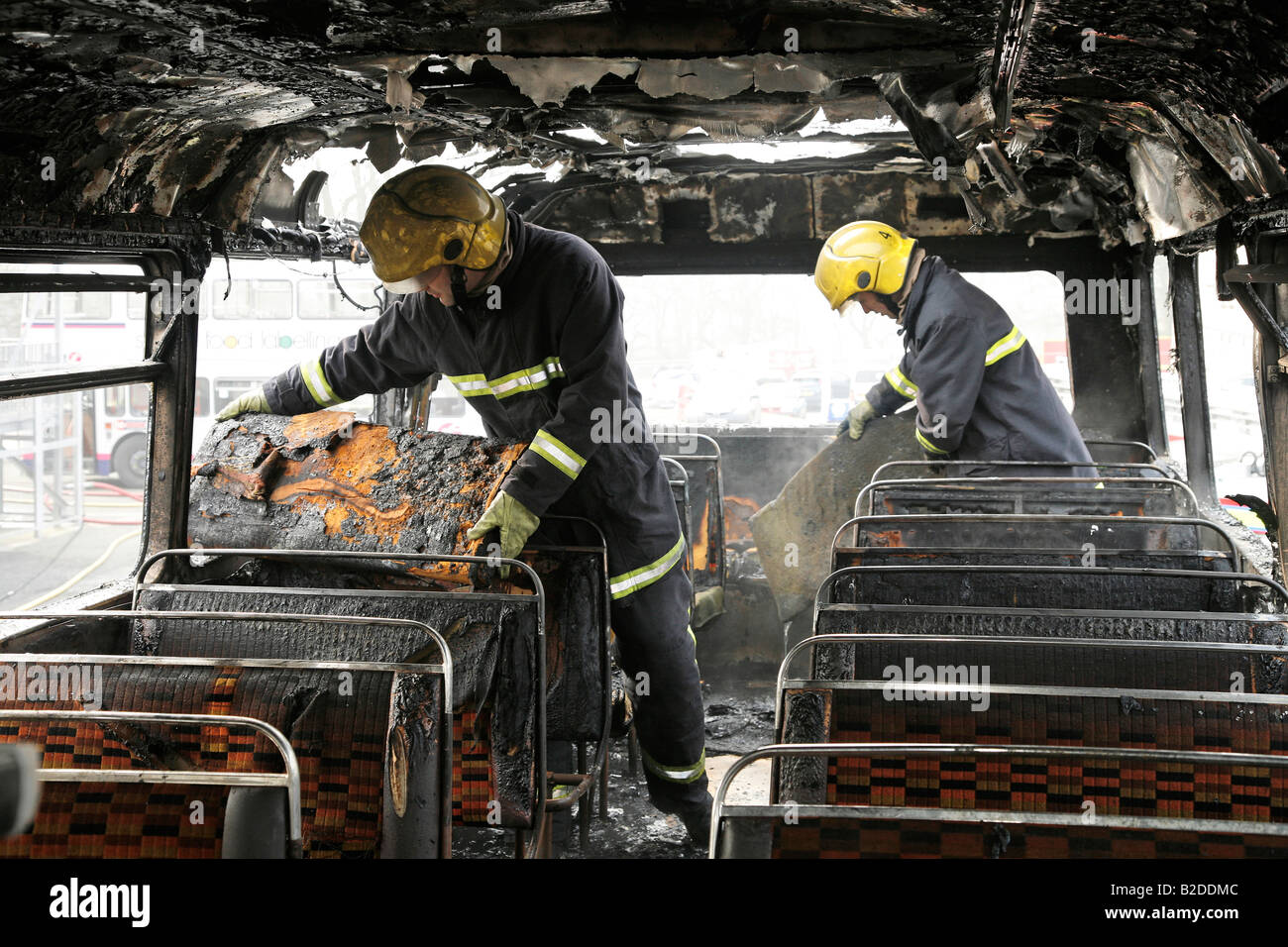 Firemen damping down and clearing fire damaged bus Stock Photo
