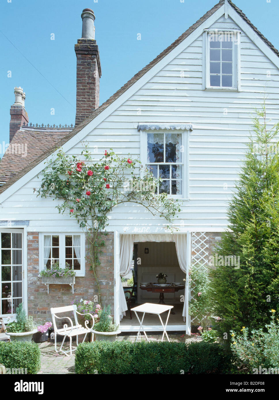 Clapboard cottage with bench and table on patio outside French doors