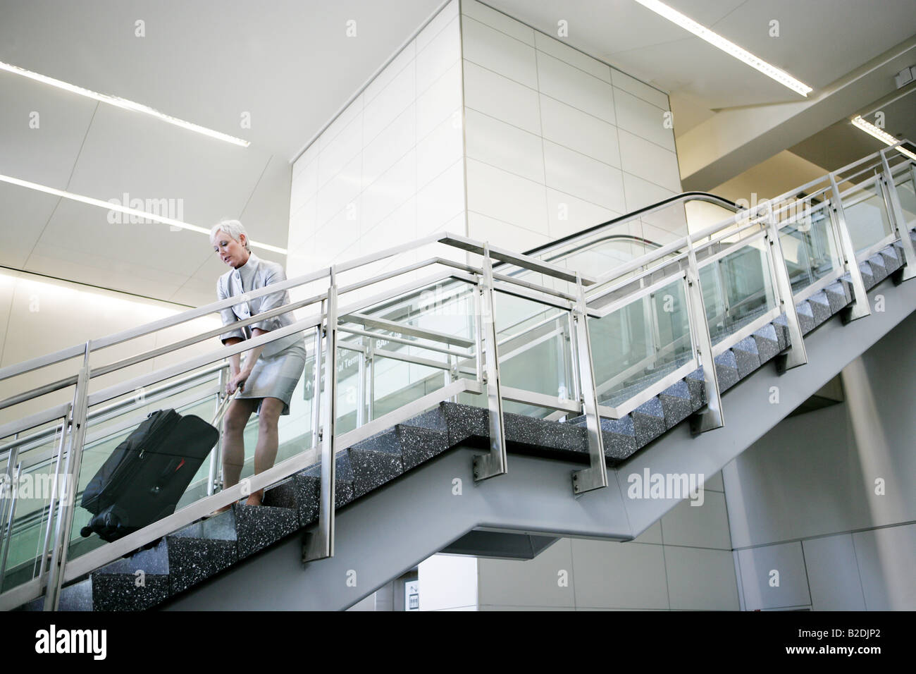 Mature woman pulling luggage upstairs in airport. Stock Photo