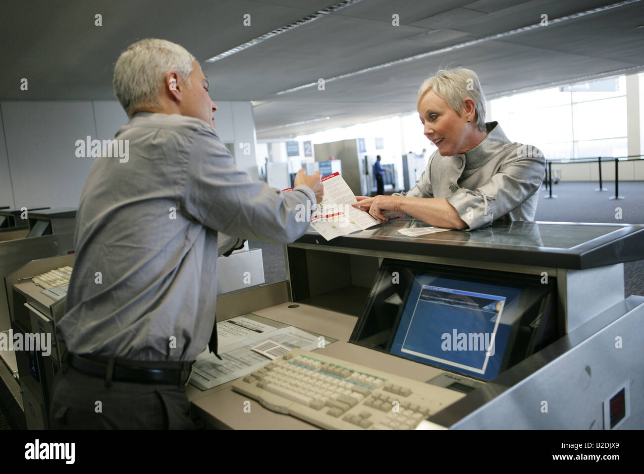 Airport attendant showing passenger brochure at check in counter. Stock Photo