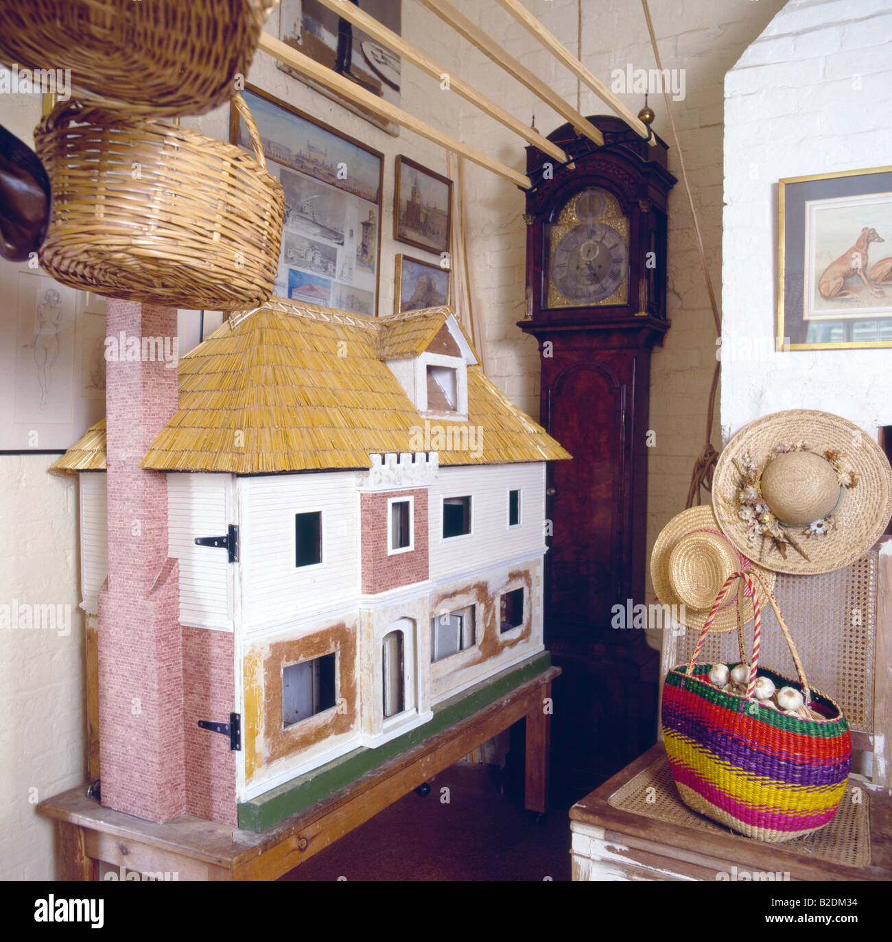 Forties dolls-house and long-case clock in corner of playroom with colorful striped basket and straw hats on chair Stock Photo