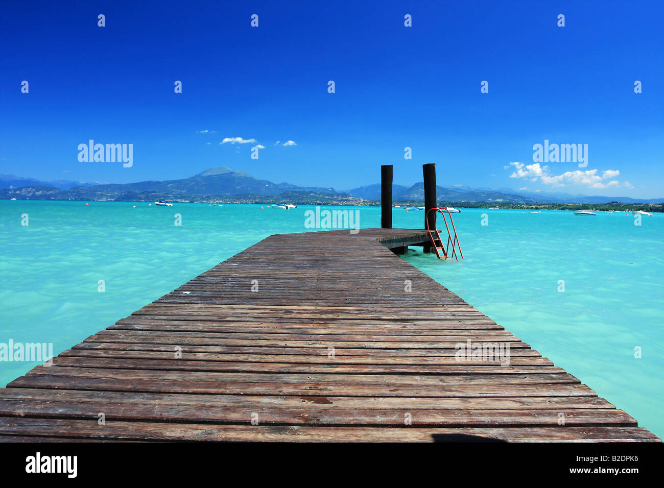 Small jetty in lake Garda Italy fantastic blue color in sky and green invitin color of water Perfect concept shot for any kind o Stock Photo