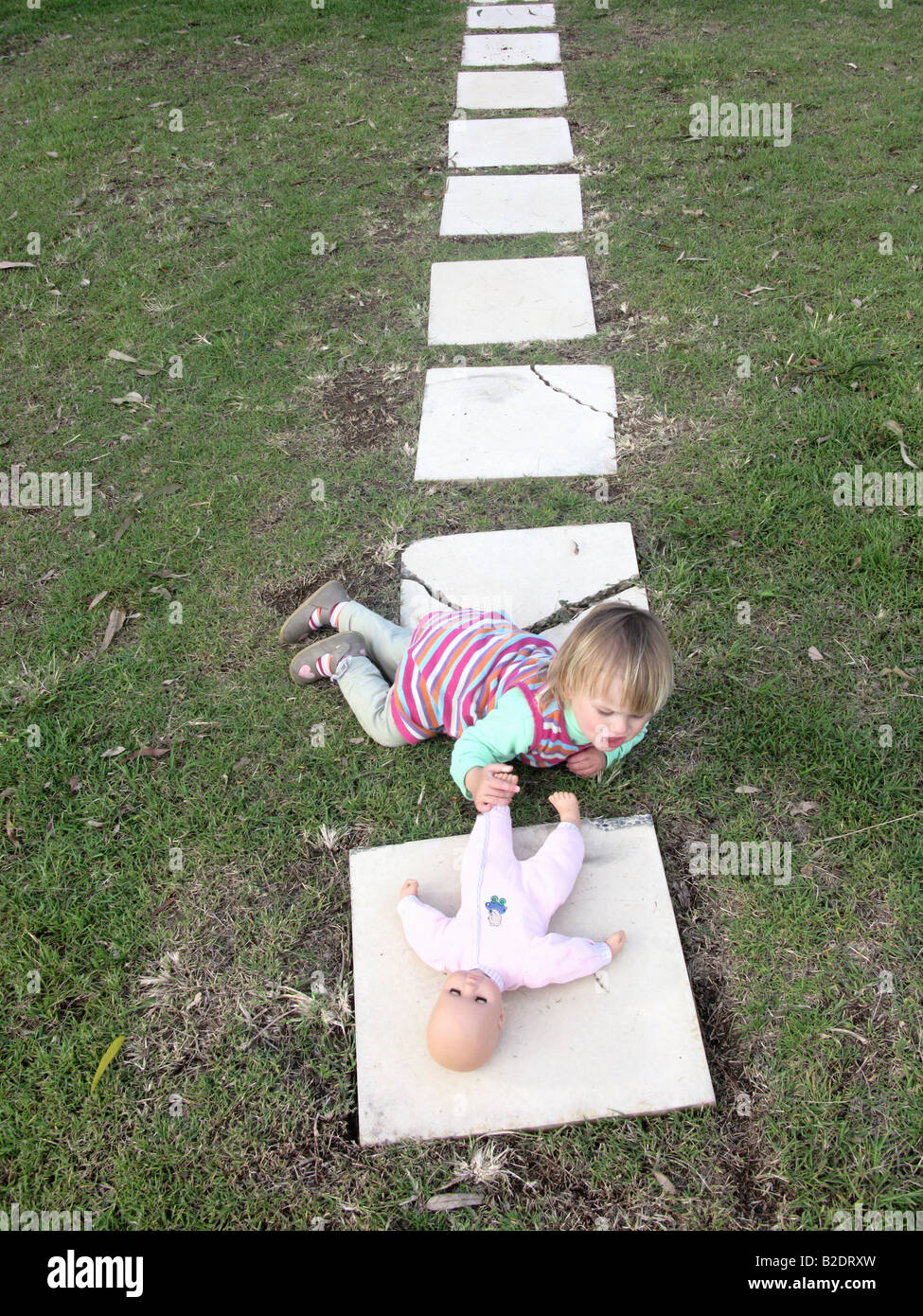 Girl playing with doll on the grass lying down Stock Photo - Alamy