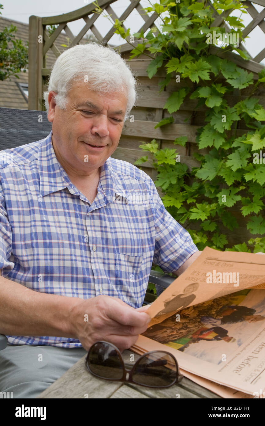 Man In 60s White Hair Reading Financial Paper In Garden Uk Stock