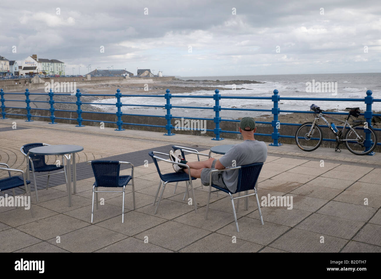 Solitary cyclist sitting on Porthcawl seafront overlooking the Severn estuary on a windy July afternoon 2008 Stock Photo