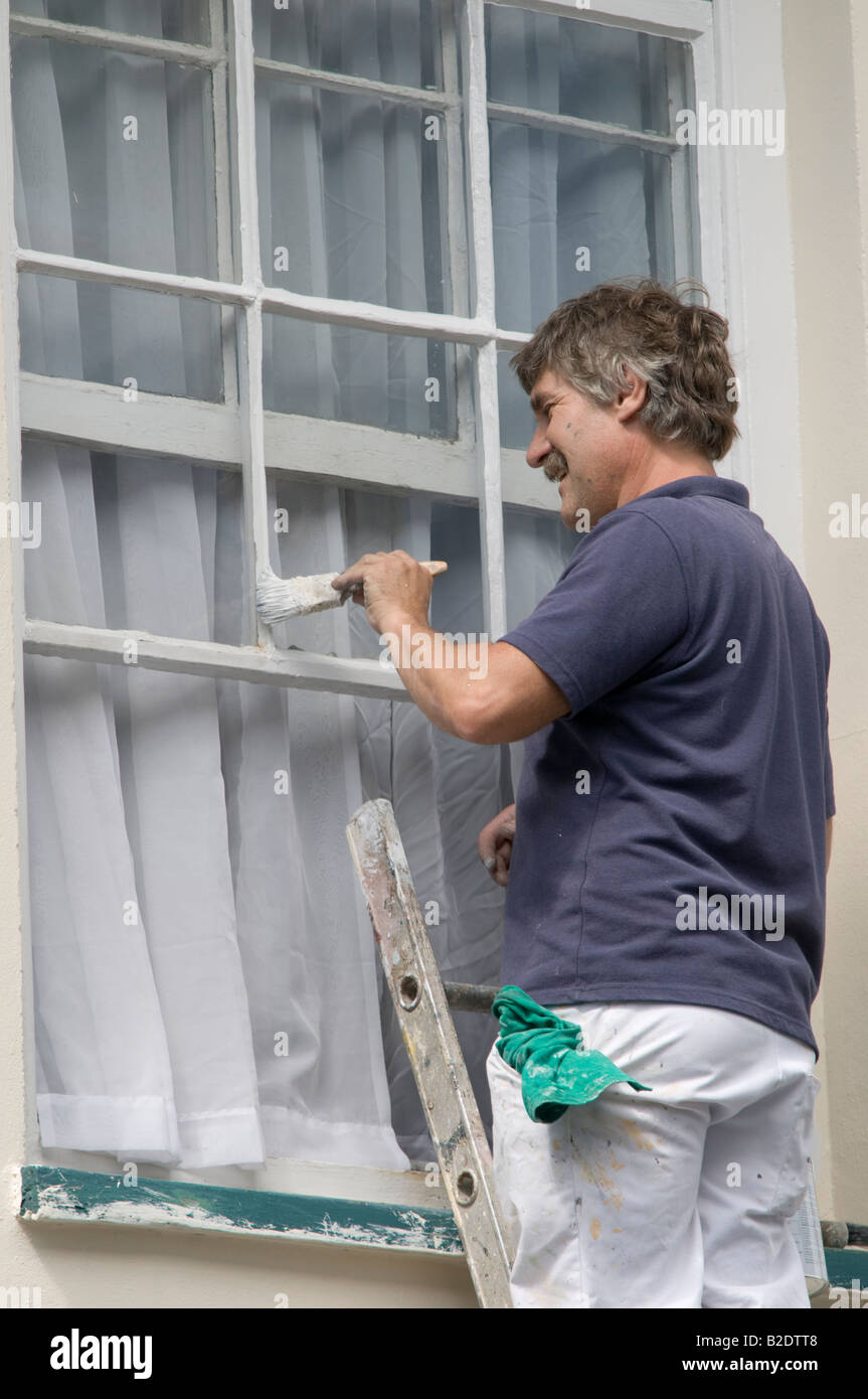 Man on ladder painting wooden sash window of a private house with white paint Stock Photo