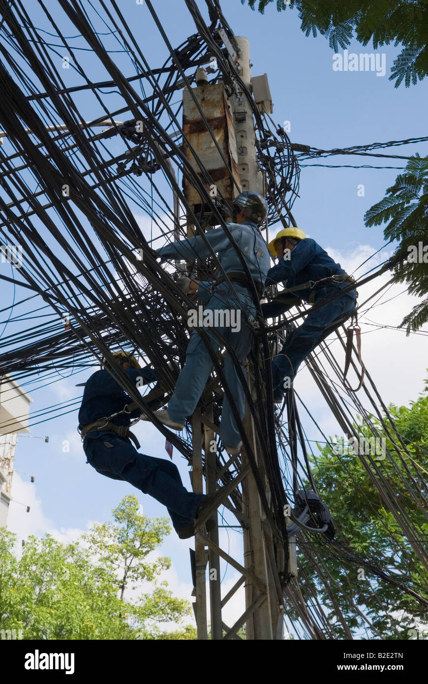 A power line maintenance crew high on a pole work on the complex tangle of electrical wires that power Ho Chi Minh City, Vietnam Stock Photo