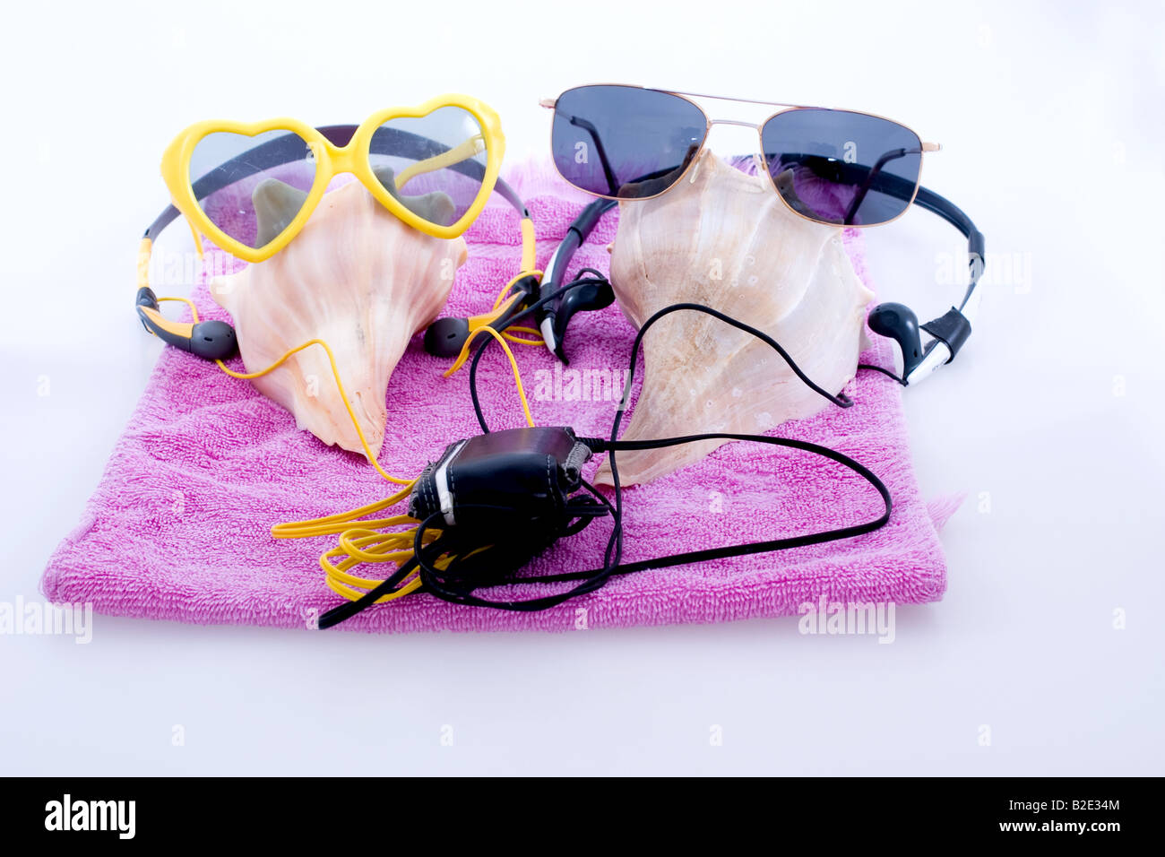 A  group of conch shells with sunglasses on a towel close together listening to an Mp3 player with headphones. Stock Photo