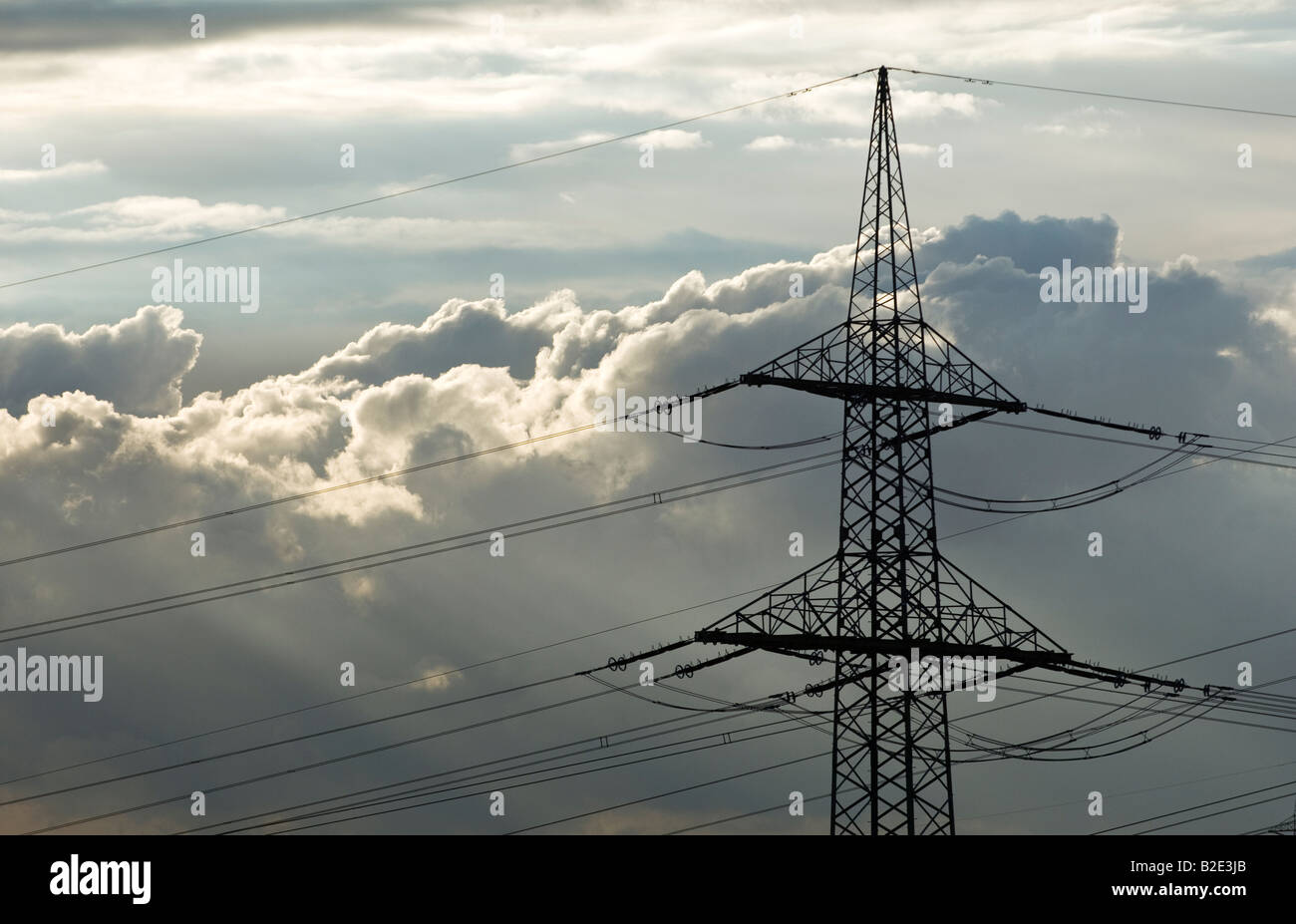 High tension electricity power cables and pylon against sunlit clouds sky Stock Photo