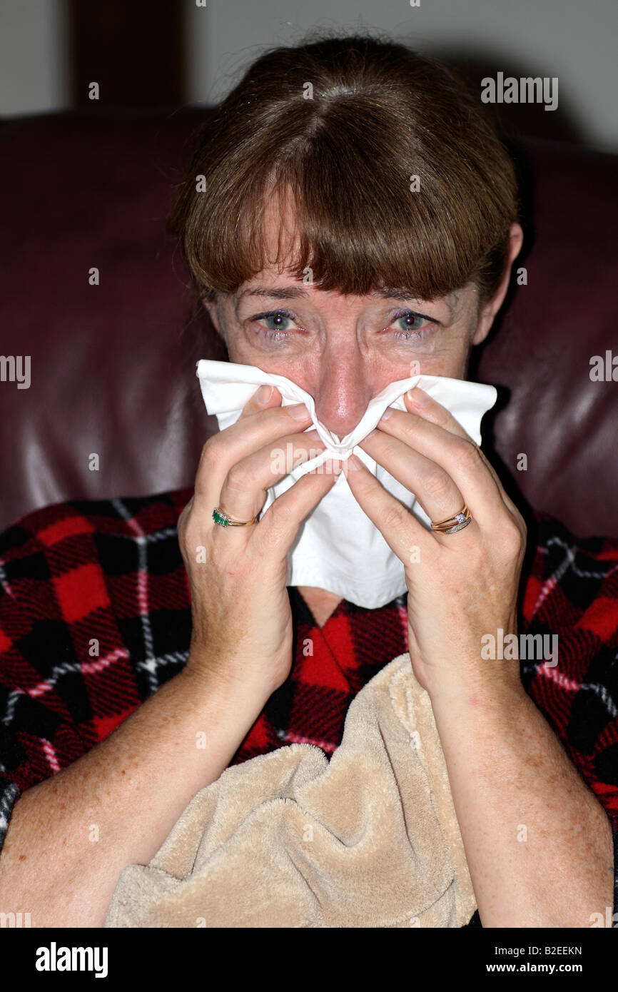 a woman looking very sick with the flu, cold or allergies sneezing and using a tissue Stock Photo