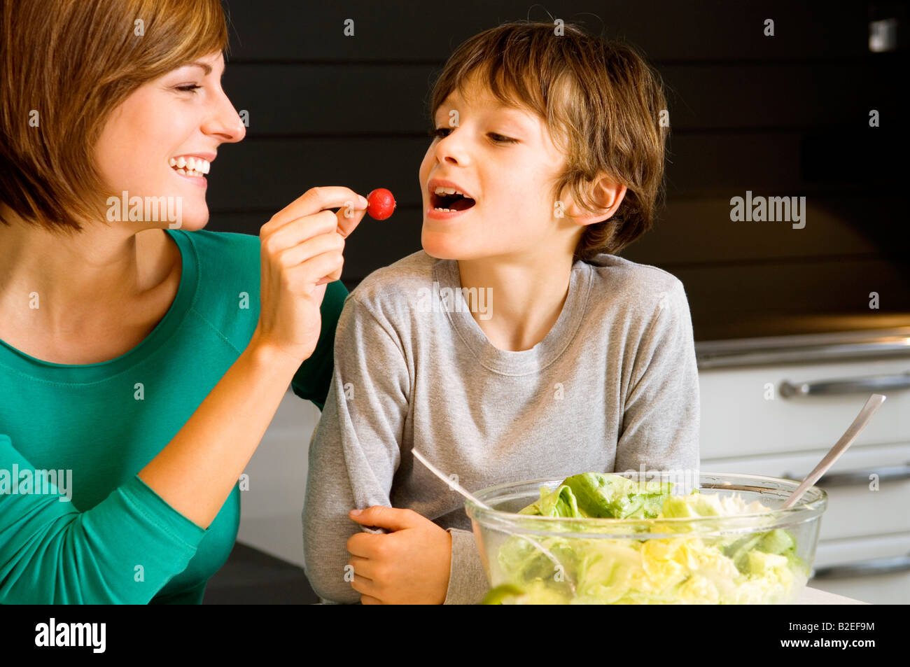 Young woman feeding a radish to her son Stock Photo Alamy
