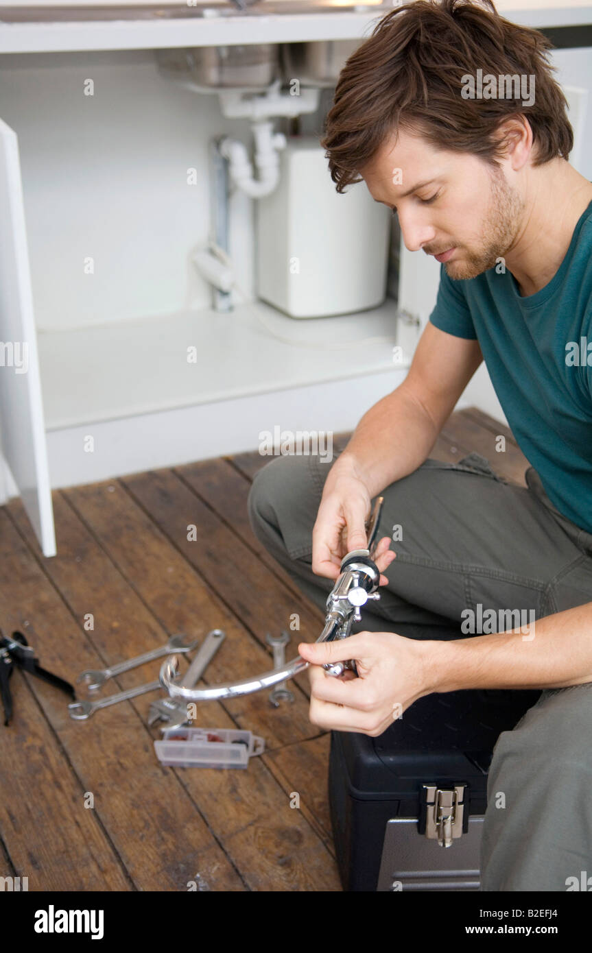 Mid adult man repairing a faucet in the kitchen Stock Photo