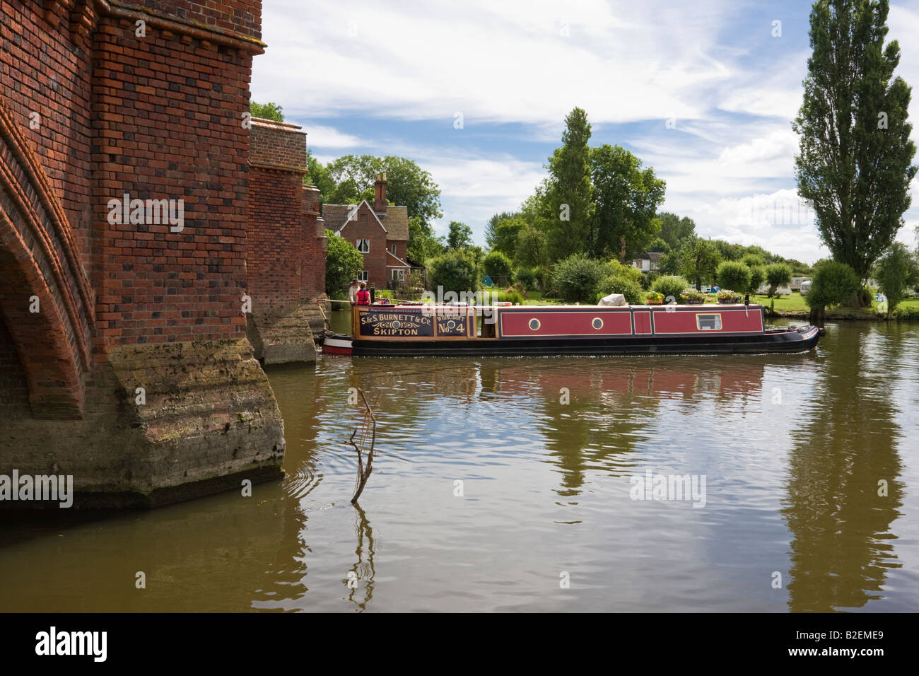 canal Boat emerges from the bridge at Clifton Hampden on the Thames Isis in Oxfordshire Stock Photo