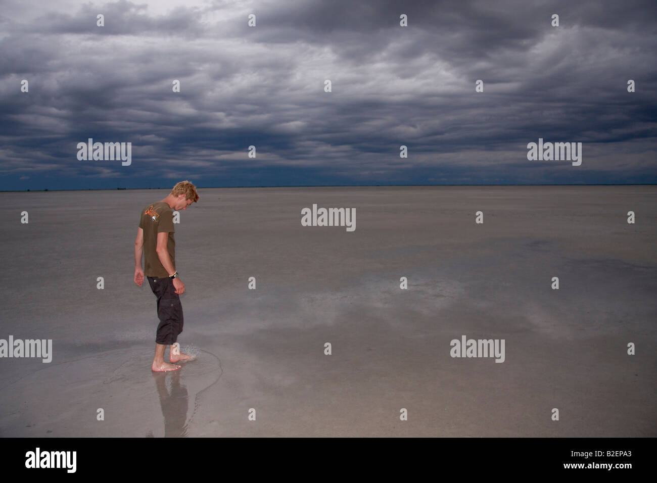 Boy walking barefoot on Makgadikgadi Pan with storm clouds overhead Stock Photo