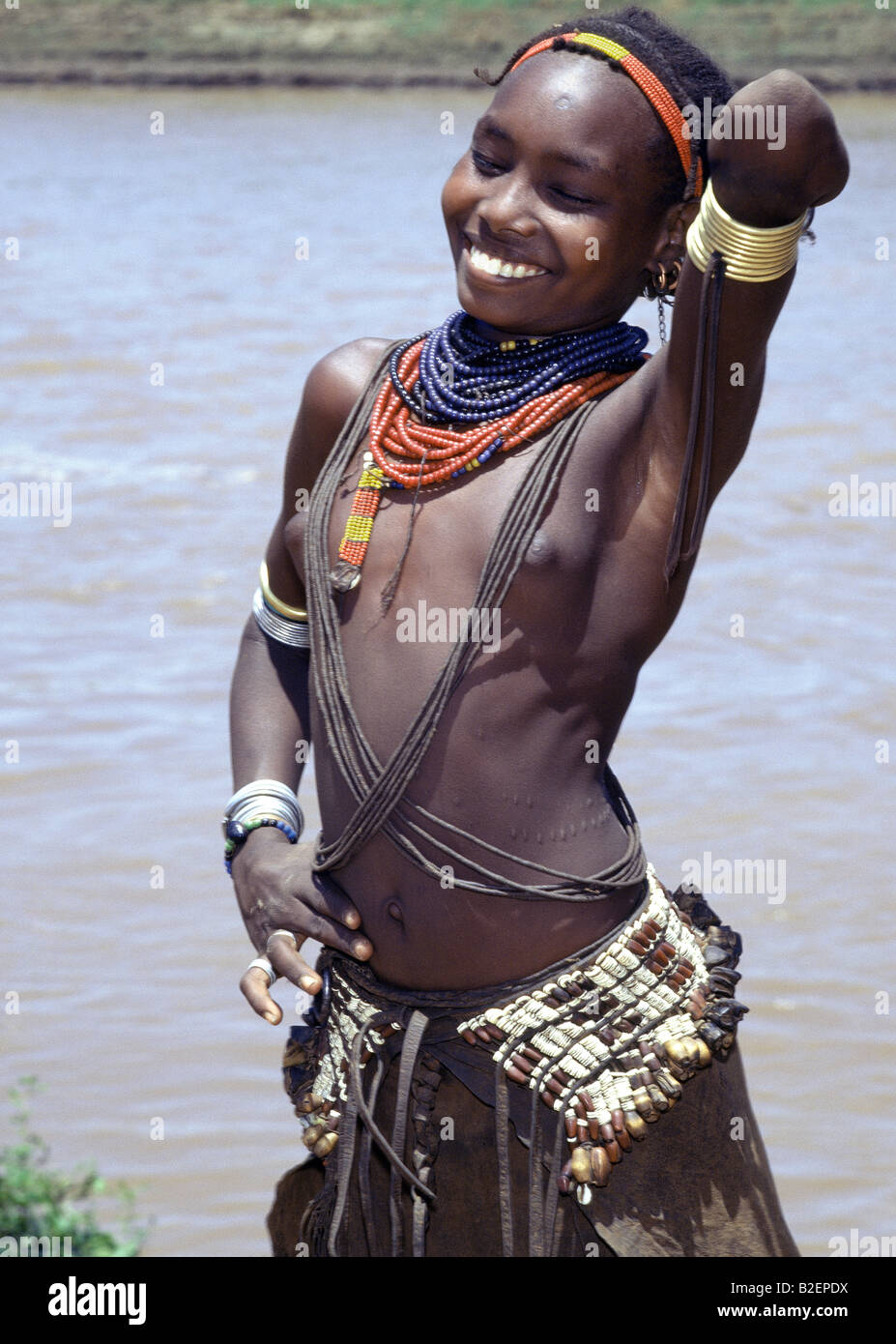 A young Dassanech girl beside the Omo River.  Her hairstyle, necklaces and metal armbands are typical of her tribe. Stock Photo